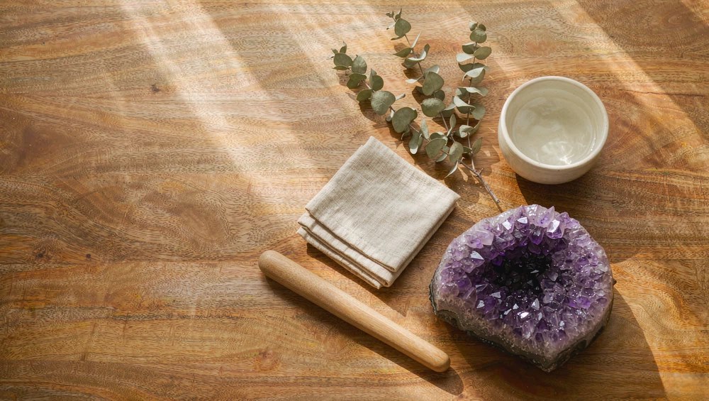 Smooth stones, paper, and a piece of purple amethyst on a warm wooden table